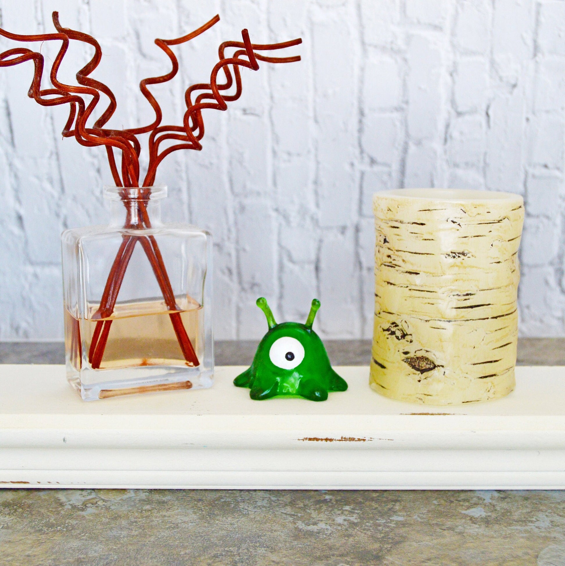 The brain slug is sitting on a small shelf between a pillar candle and a reed diffuser.